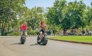 Two girls having fun and cruising around after finding E-Magine Tours by searching for “scooter rental near me.”