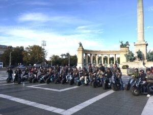 A group of men sitting on an E-scooter at Heroes’ Square in Budapest
