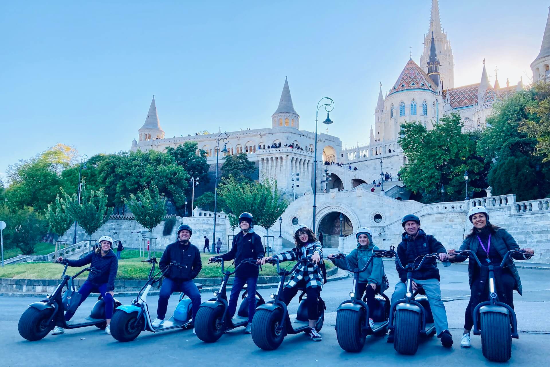 Un groupe de personnes posant sur des scooters électriques lors d'une visite du château de Buda