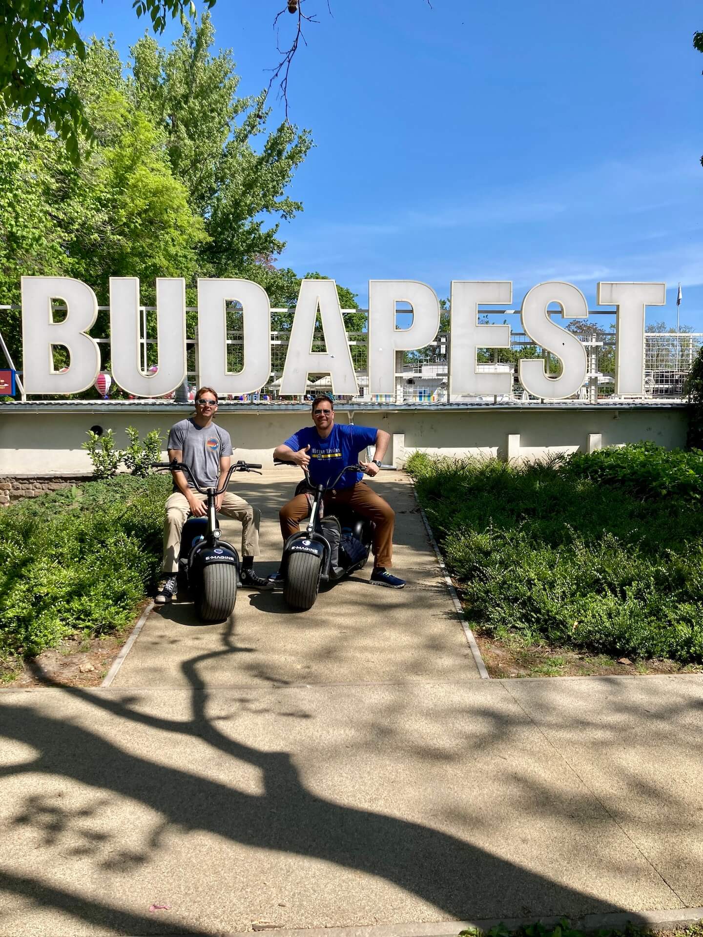 Jeunes en visite privée en scooter électrique devant le panneau Budapest