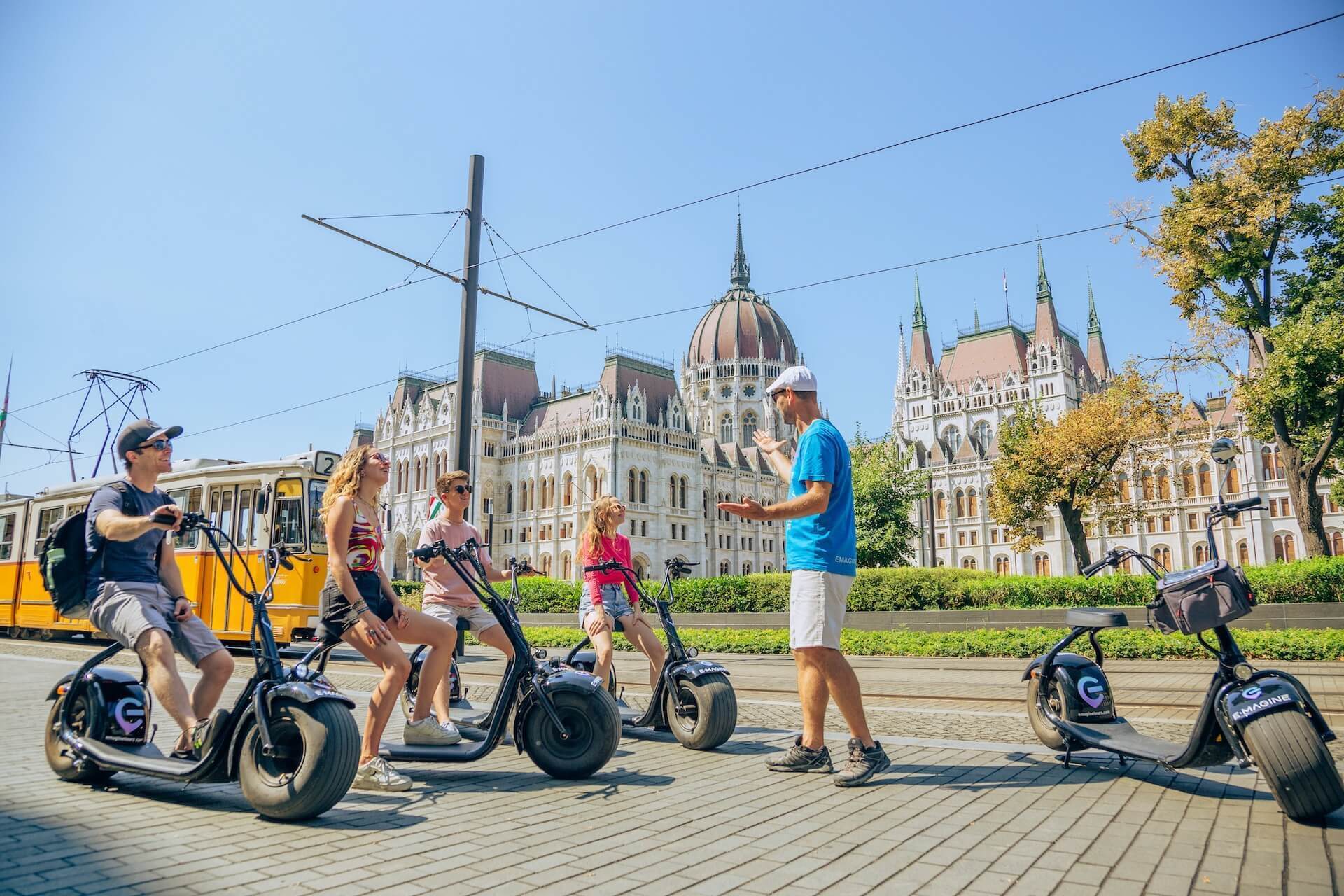 a group of people on electric scooters in front of the Parliament in Budapest.