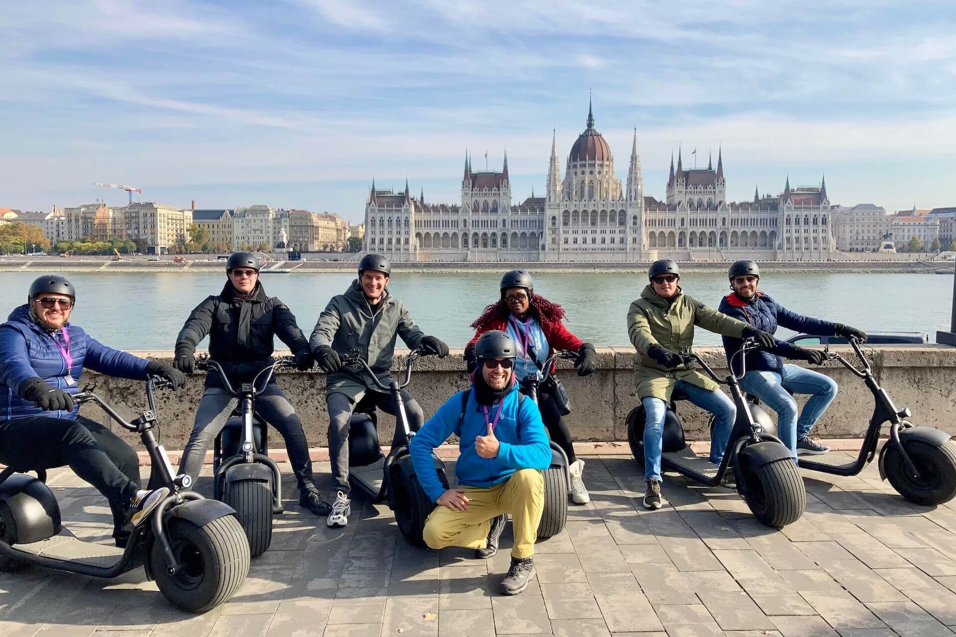 Des personnes lors d'une visite en scooter électrique posant avec le Parlement en arrière-plan.