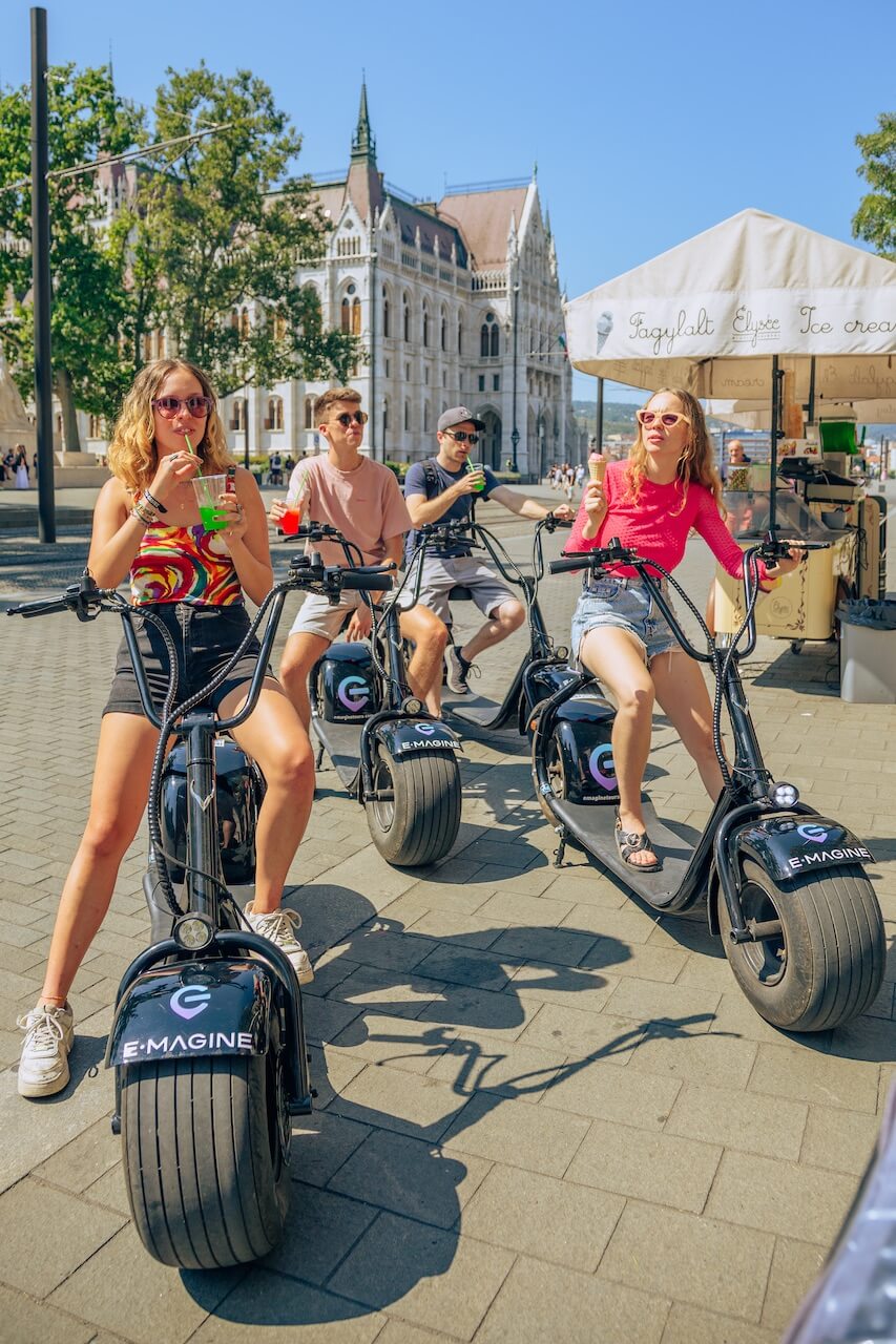 Des jeunes sur des scooters électriques s'arrêtant pour une boisson fraîche par Budapest Parliamanet